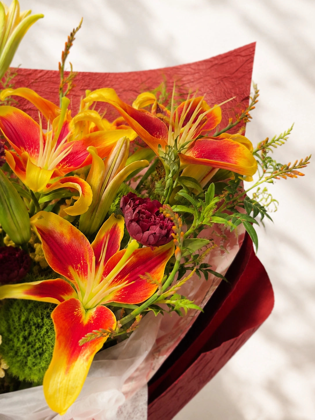 Amber Flame 側角 close-up，橙色 lilies 配酒紅包裝紙，展現豐富花材層次，elegant congratulation bouquet.