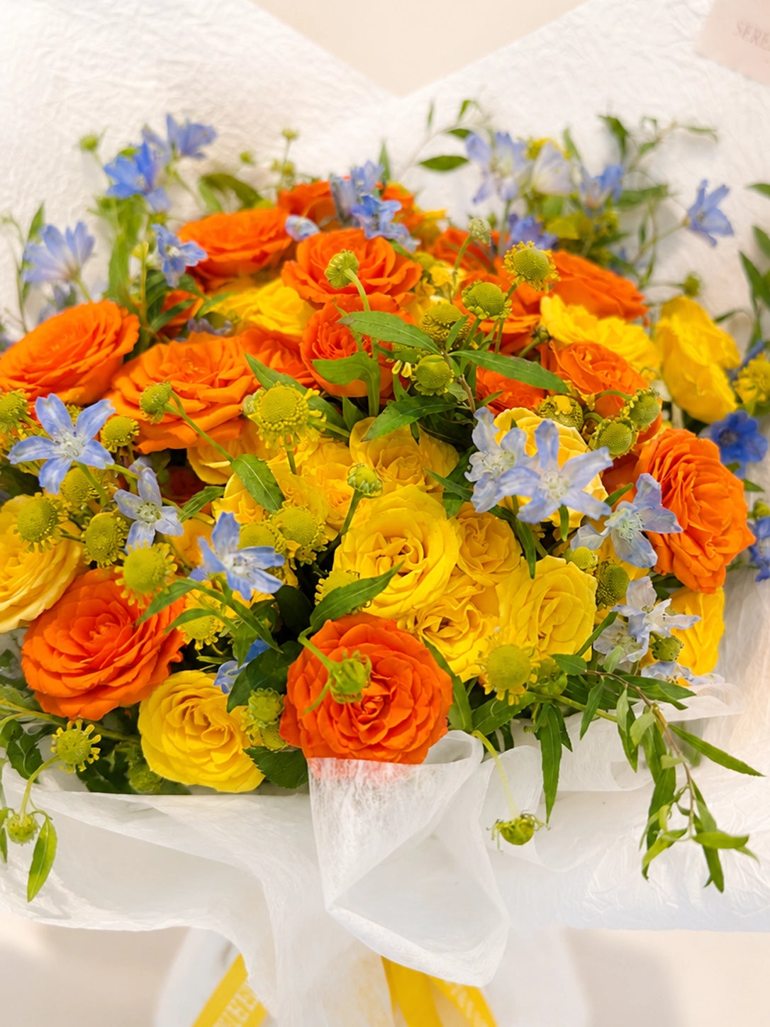 For You, Always 橙色玫瑰、黃色花材及藍色季節花自然交織，cheerful bouquet celebrating new beginnings and joyful moments.
