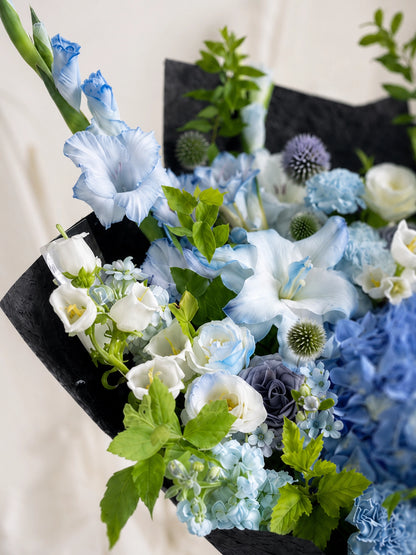 Midnight Voyage close-up，展示淡藍 gladiolus、藍白花材及黑色質感包裝