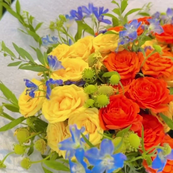 Where Light Begins bouquet 360° video，多角度展示橙色玫瑰、金黃色花材及藍色季節花，bright floral arrangement inspired by hope, light and beautiful new chapters.